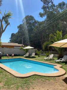 a swimming pool in a yard with chairs and umbrellas at Spacious Beach House with Pool for Relaxing in El Quisco