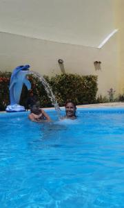 dos personas en una piscina con una fuente de delfines en Pousada Jesmar, en Praia do Frances