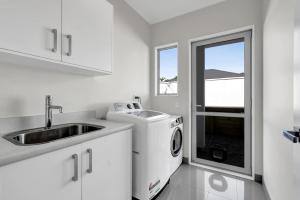 a white kitchen with a sink and a washing machine at Executive On Parkview - 3BR modern family home in New Plymouth +23 photos
