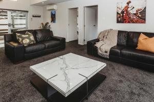 a living room with a black leather couch and a glass table at Love It On Lemon - modern townhouse near CBD in New Plymouth