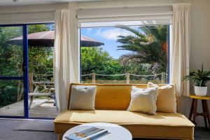 a living room with a yellow couch and a sliding glass door at Butlers Studio Two in Oakura