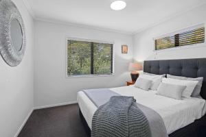 a white bedroom with a large bed and two windows at Seven By The Sea - stylish apartment near port in New Plymouth