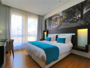 a hotel room with a bed, desk and a painting on the wall at Jupiter Lisboa Hotel in Lisbon