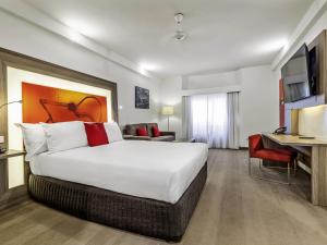 ein Hotelzimmer mit einem großen Bett und einem Schreibtisch in der Unterkunft Novotel Darwin CBD in Darwin
