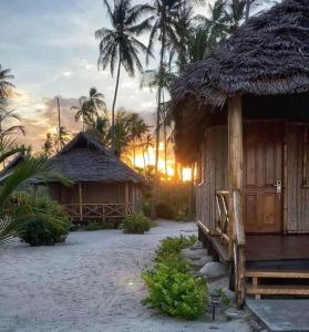 a couple of huts on the beach with the sunset at Barry's Beach Resort Pangani in Mkwaja