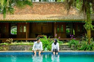 two people sitting in a pool in front of a house at Katumbiri Resort and Villa by Tripletree in Bogor