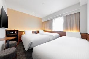 a hotel room with three beds and a television at Sotetsu Grand Fresa Osaka-Namba in Osaka