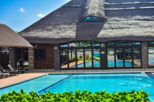 a resort swimming pool with a thatched roof at MKHUZE INN in Mkuze