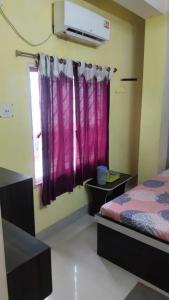 a room with a bed and a window with purple curtains at priyadarshi in Digha