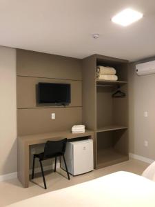 a bedroom with a chair and a tv on a wall at Hotel Seville Comfort in Telêmaco Borba