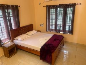 a bedroom with a large bed with white sheets and windows at Cozi Rooms in Varkala