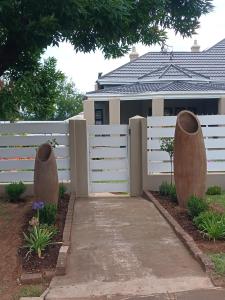 a white fence with two large vases next to a sidewalk at Maison De Blom in Aliwal North