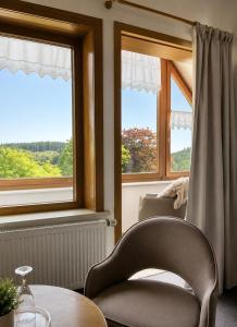 ein Stuhl und ein Tisch in einem Zimmer mit Fenstern in der Unterkunft Hotel Daheim in Gehlberg