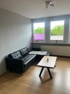 a living room with a black leather couch and two windows at Wohnung Ton Strand in Fehmarn +5 photos