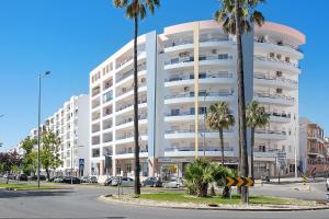 a large white building with palm trees in front of it at Rei Apartment in Quarteira