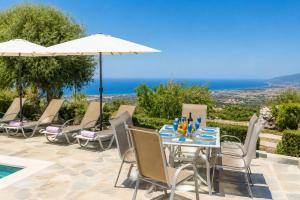 a table with chairs and an umbrella next to a pool at Villa Panorama Tessera in Drousha
