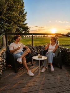 two people sitting in chairs on a deck with the sunset at Bed&Bus met dakterras in Rucphen
