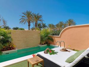 a patio with a table and a pool with palm trees at Green Garden Eco Resort in Playa de las Americas