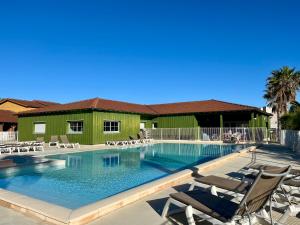 a swimming pool with chairs and a green building at Résidence Lagrange Vacances La Grenadine in Marseillan