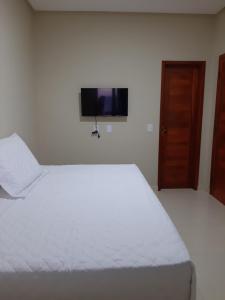 a bedroom with a white bed and a flat screen tv at Pousada Makai - Cajueiro da Praia in Barra Grande