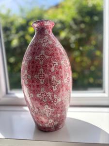 a red vase sitting on a table in front of a window at Ferienwohnung Zeitweise in Bünsdorf am Wittensee in Bünsdorf