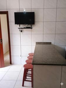 a kitchen with a counter with stools and a tv on the wall at Residencia Siqueira in Garopaba