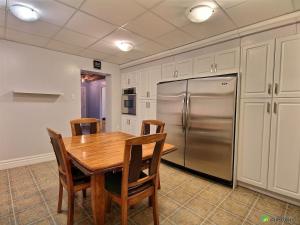 a kitchen with a wooden table and a stainless steel refrigerator at La Tour Boisée with Private Spa & Pool, Pool Table in Sainte Béatrix