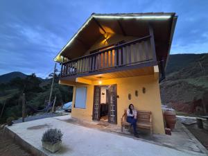 a woman sitting on a bench in front of a house at Chalé Recanto da Grota in Passa Vinte
