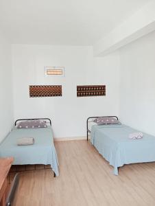 two beds in a room with white walls and wooden floors at Appart Chris Mindelo in Mindelo