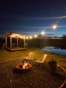 a fire pit with two chairs and a cabin at night at Cabana de teto de vidro in Santa Cruz do Sul