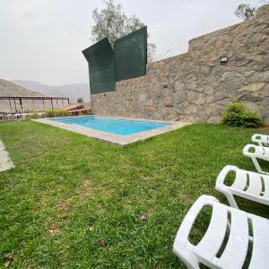 a pool with two white chairs in the grass at La casa del cuadro in Lima