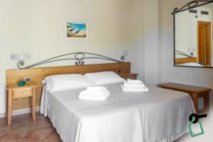 a bedroom with a bed with white sheets and a mirror at Hotiday Cala Gonone in Cala Gonone