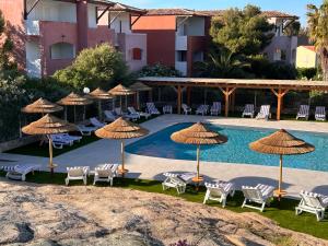 a pool with chairs and umbrellas next to a hotel at Hôtel Maristella in Algajola