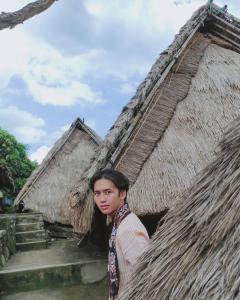 a man standing in front of a thatched building at Greentea Hostel in Labuhanhaji +7 photos