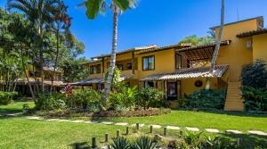 a yellow house with palm trees and a yard at Pousada Villa Bianca in Arraial d'Ajuda