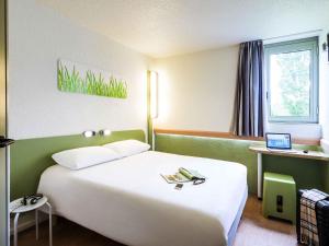 a bedroom with a large white bed with a laptop at ibis budget Châtellerault Nord in Châtellerault