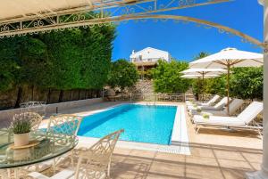 a swimming pool with chairs and a table and an umbrella at Villa Golden Tiara Large Private Pool AC WiFi in Corfu
