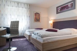 a hotel room with two beds and a chair at Hotel Villa Sulmana in Neckarsulm