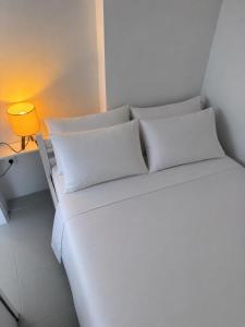 a white bed with white pillows and a yellow lamp at Seaside Serenity in Komi Beach! in Kómi