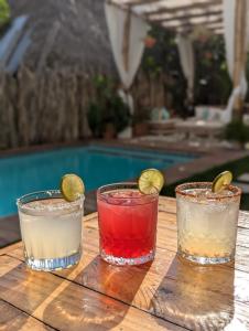 three cocktails on a wooden table next to a pool at Wander Boutique Hotel in El Paredón Buena Vista