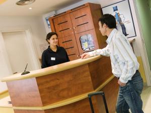 a woman standing behind a counter with a man standing at at ibis budget Bar le Duc in Bar-le-Duc