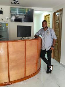 a man standing next to a wooden desk with a television at Hotel Riviera del Atrato in Bojayá