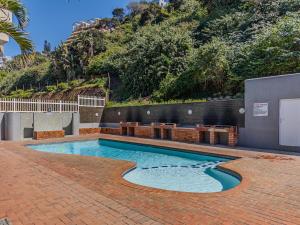 a swimming pool on a brick patio with a hill at Rustic Beachfront Apt! Shared Pool! in Umdloti