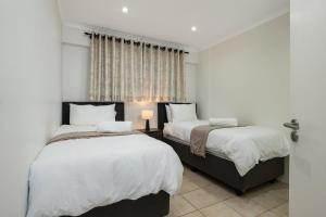 two beds in a bedroom with white walls and a window at Rustic Beachfront Apt! Shared Pool! in Umdloti +9 photos