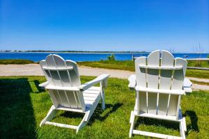 two white chairs sitting on the grass near the water at Barnstable Harbor Home in Barnstable