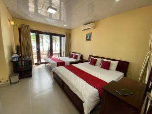 a hotel room with two beds and a desk and window at Beachfront Bungalow Cuu Long in Phú Quốc