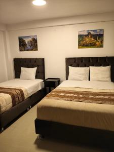 a bedroom with two beds and paintings on the wall at Hostal Ñustas INN in Machu Picchu
