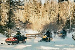 three people riding on snowmobiles in the snow at Shady Lane Lodge in Eagle River
