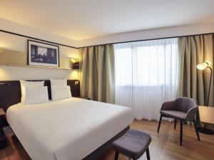 a hotel room with a large white bed and a chair at Mercure Paris Saint-Ouen in Saint-Ouen