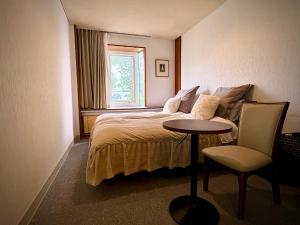 a bedroom with a bed and a table and a chair at Pension Puutaro in Zaō Onsen